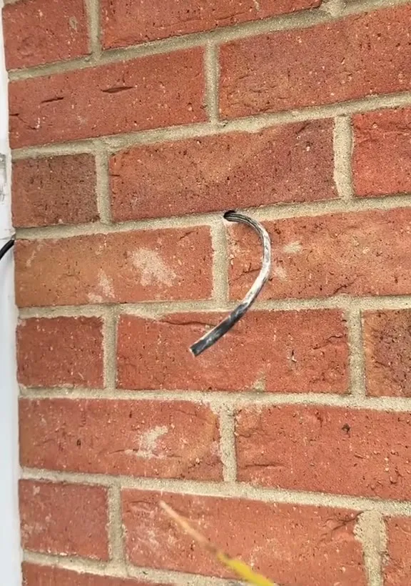A steel draw wire coming out of a mortar joint in a red-brick wall