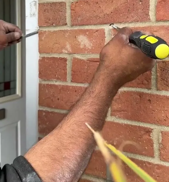 Marking the drill point on a brick wall with a pencil, a tape measure held against the door frame