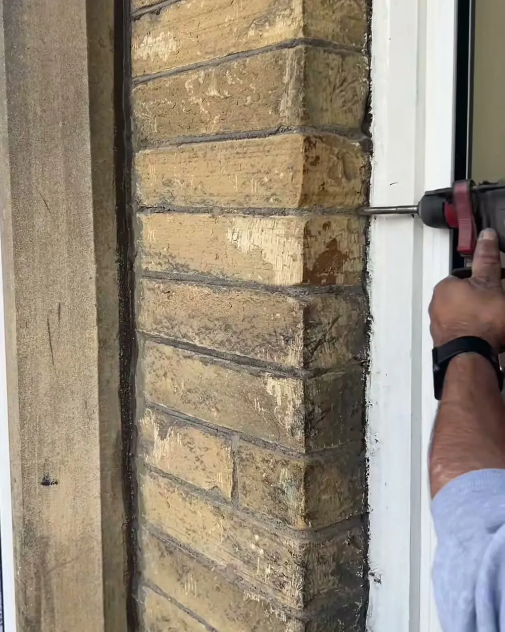 A drill going into the mortar line of a stone wall beside a white window frame