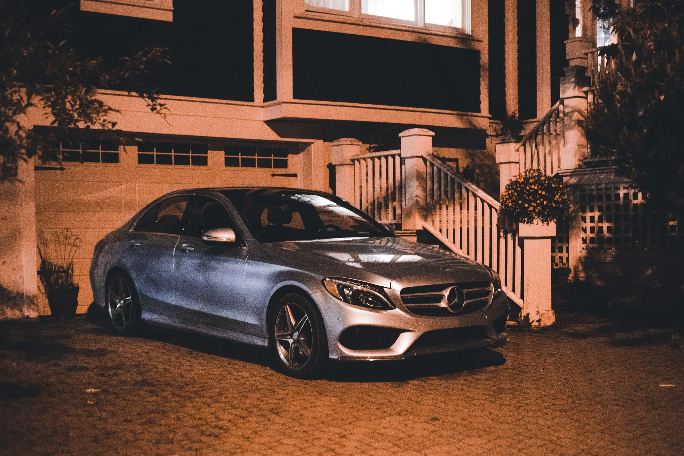 A silver car on a block-paved drive at night, lit warm and in full colour