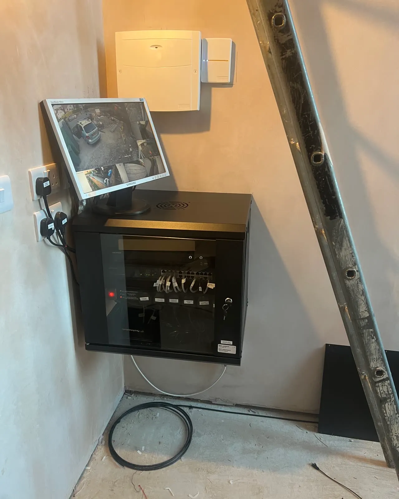 A wall cabinet with the CCTV recorder inside and a monitor on top, the new double socket fitted on the plastered wall beside it