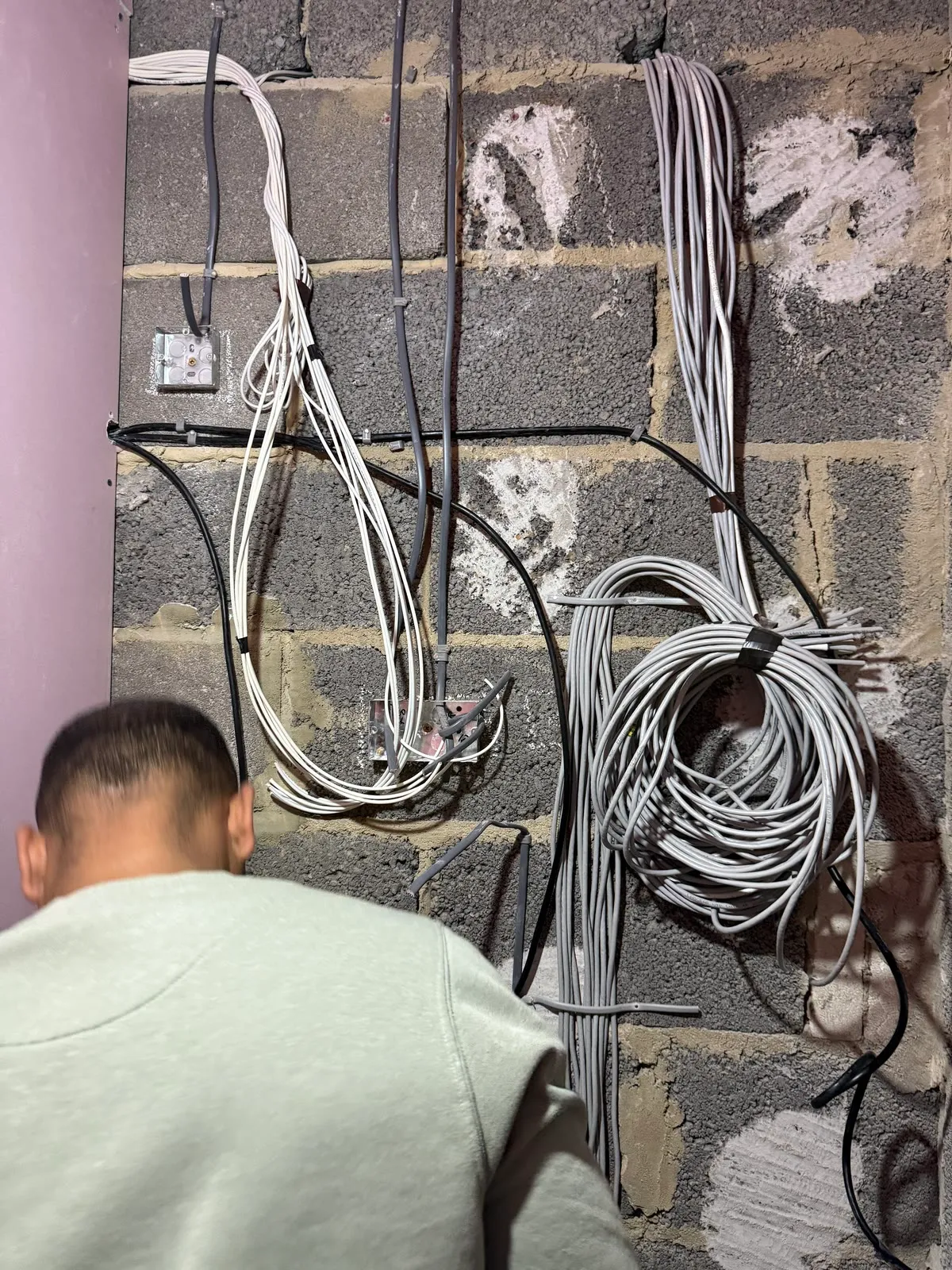 Bundles of grey data cable dressed against a block wall at first fix, each run labelled and coiled