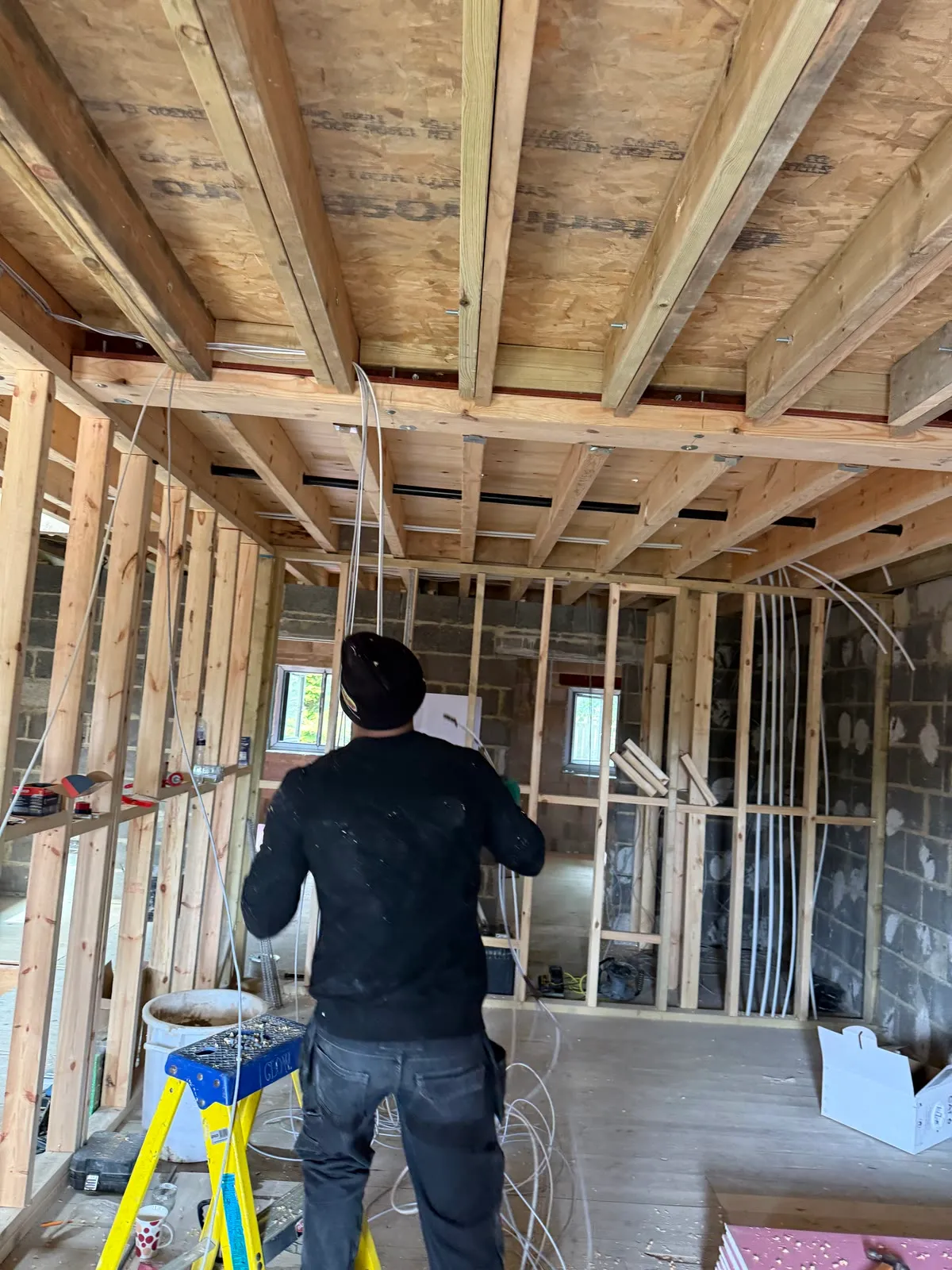 Mitu in the open timber frame of a new build, cables run through the joists above him