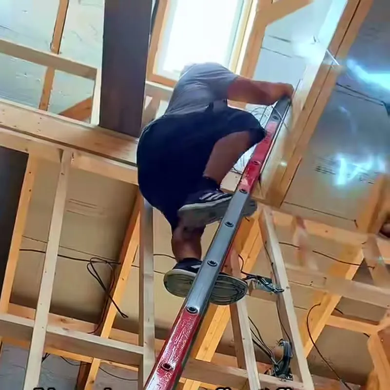 Mitu up a ladder in the open timber frame of a new build, running cable through the joists