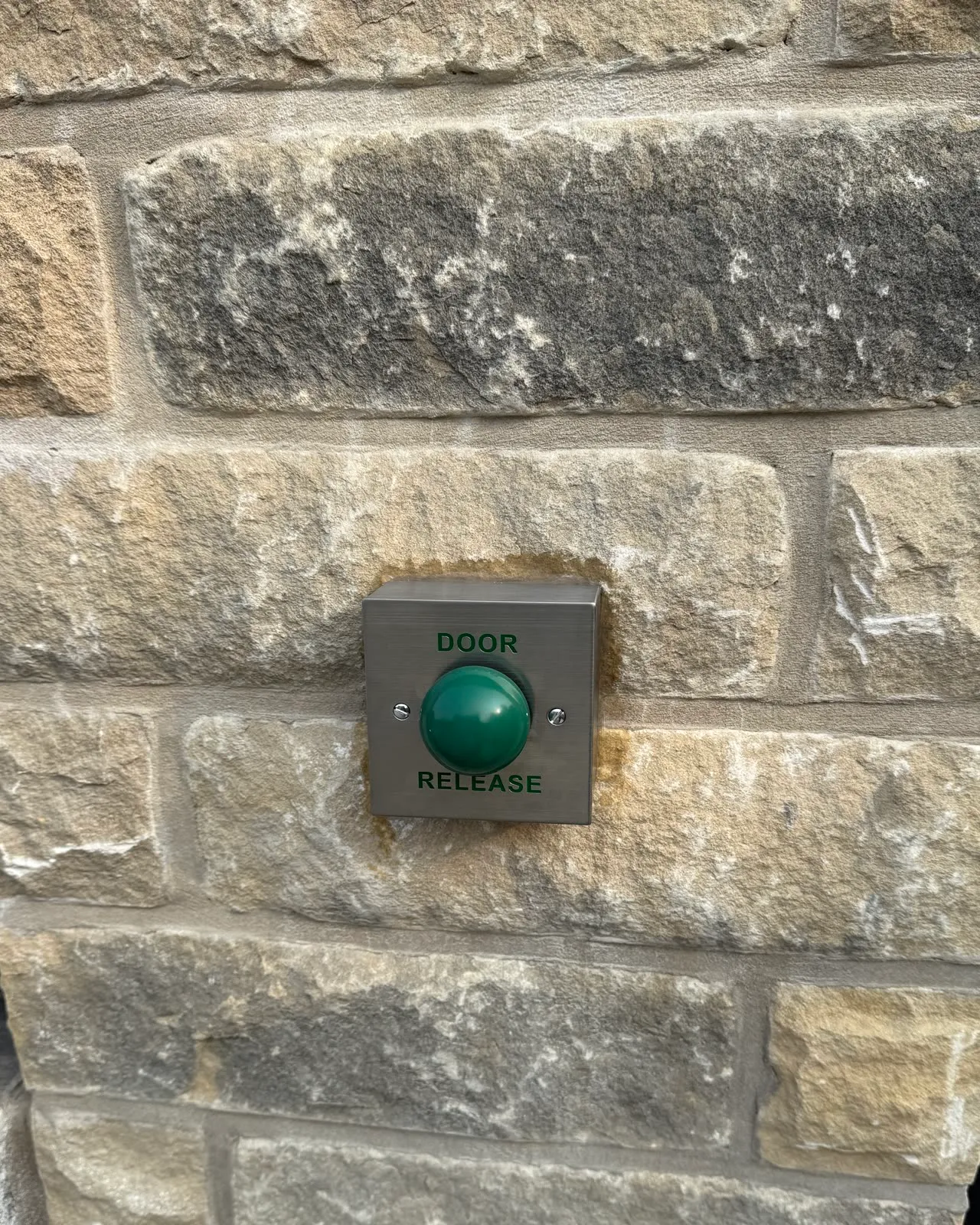 A green Door Release button on a stainless plate, set flush into a stone gate pillar