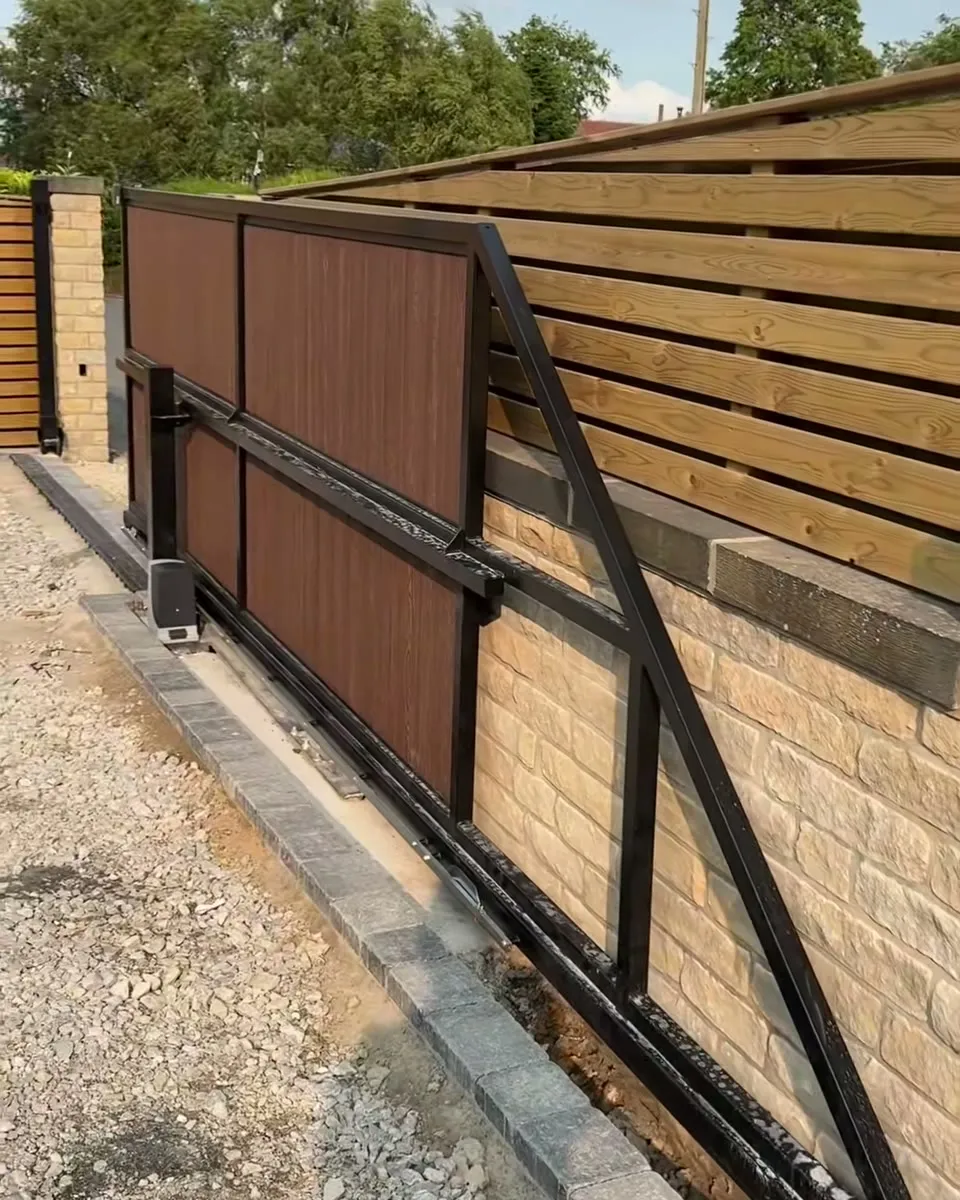 A new sliding electric gate on a gravel driveway, the motor at the foot of the gate and a stone pillar at the far end