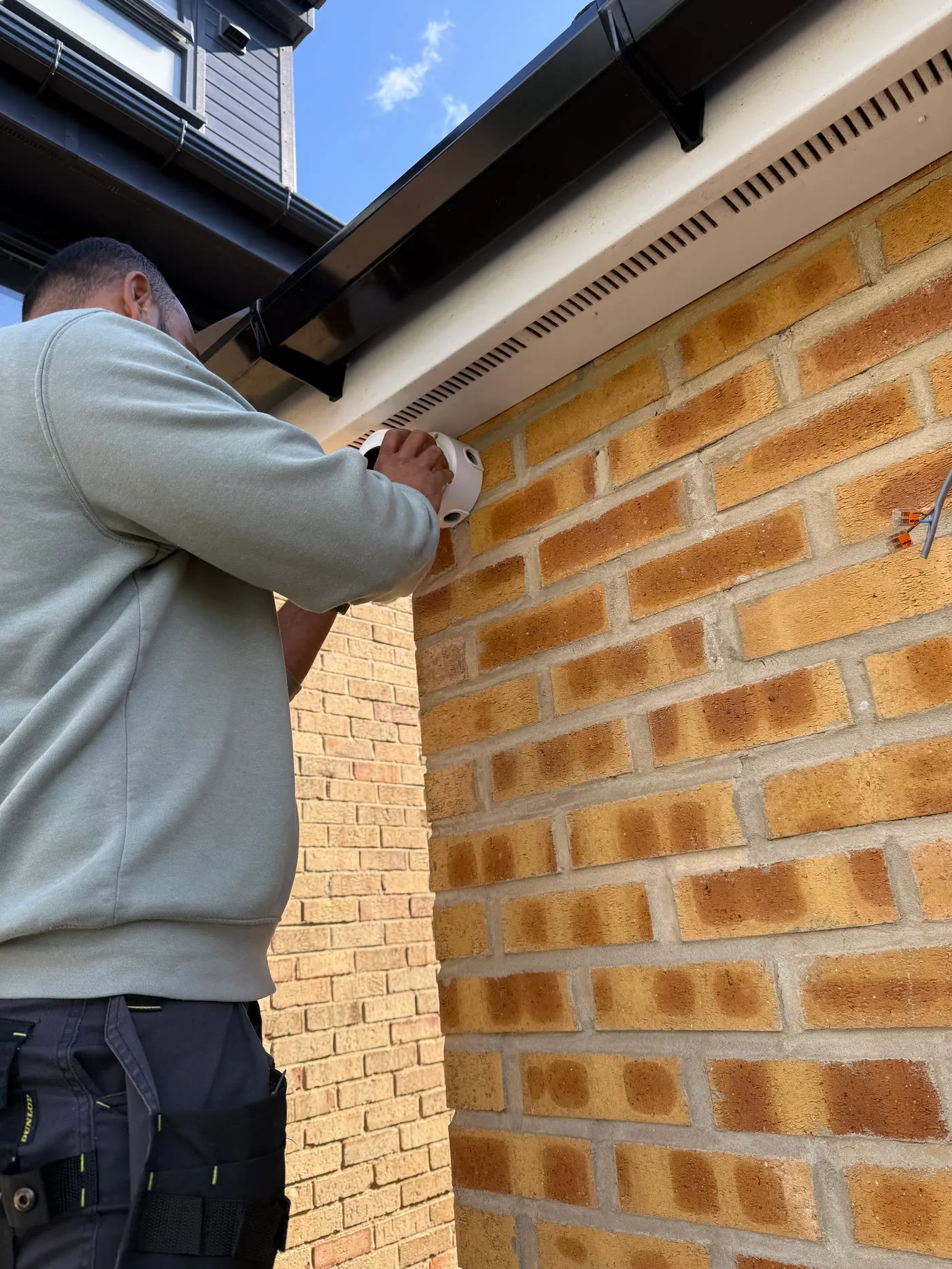 Mitu fitting a Hikvision turret camera under the soffit of a brick house, cable already inside the wall