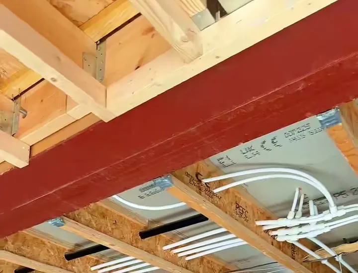 Looking up at the joists of a new build at first fix, a black cable run through them beside the pipework