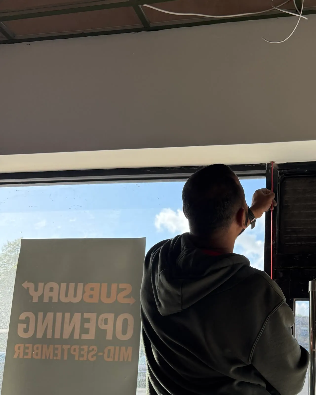 Mitu on a stepladder at the shop window, the Subway opening sign on the glass behind him