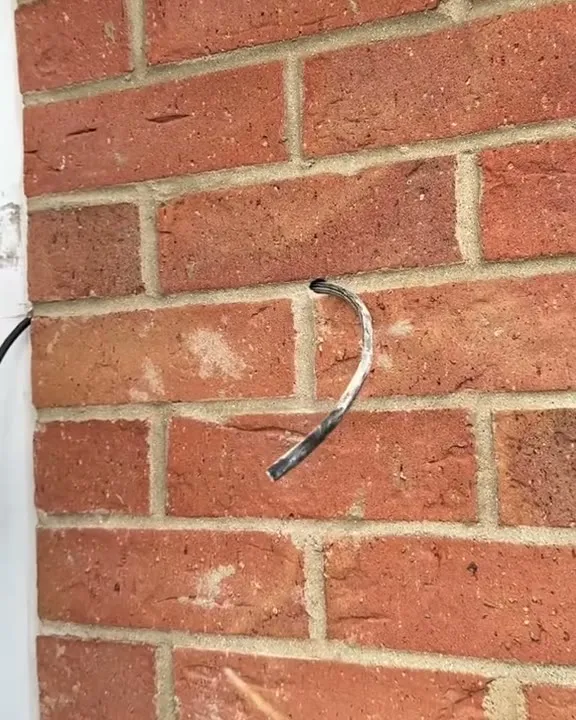 A single cable end poking out of one neat hole in the mortar line of a red-brick wall