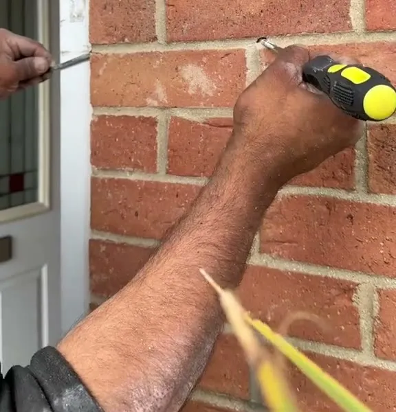 A tape measure held against the brickwork by the door frame, marking where the hole will go
